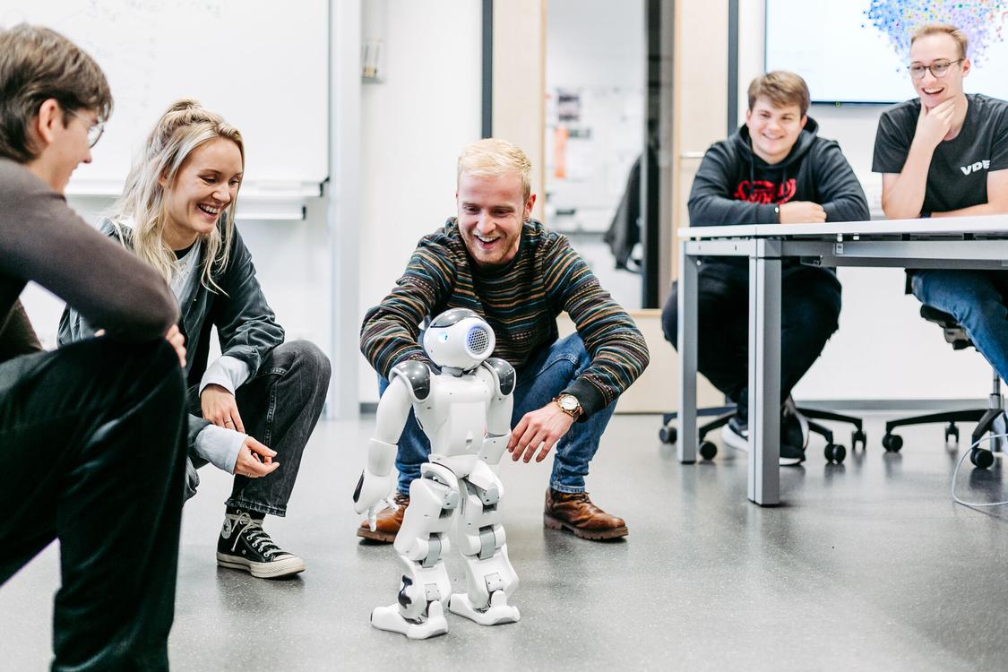 Studierende arbeiten mit einem kleinen Roboter.